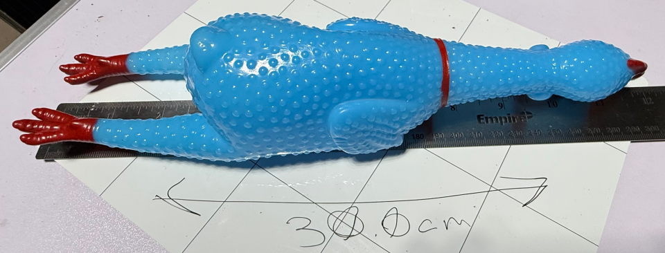 A blue rubber chicken laying on top of a ruler which is laying on top of a white board. The white board shows that the rubber chicken measures 30.0cm in length.