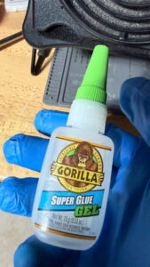 My hand wearing a blue glove holding a bottle of Gorilla Glue Super Gel.