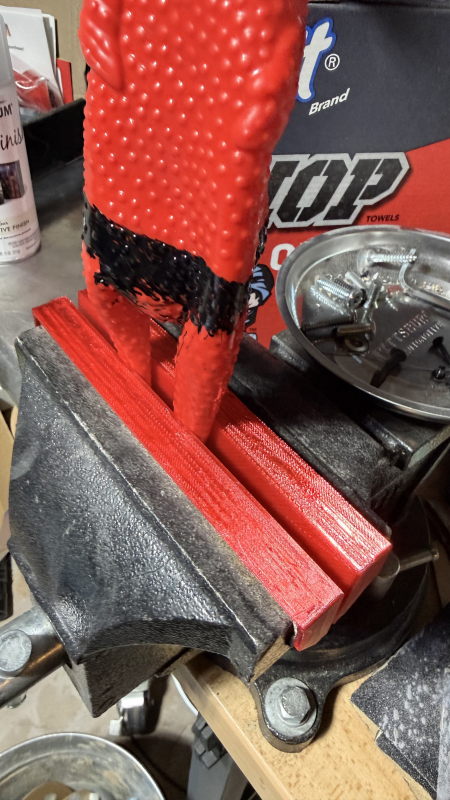 A red rubber chicken in a vise sporting some pretty red jaw covers.